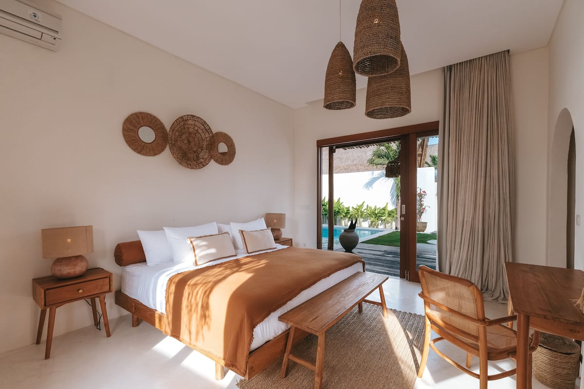 A bedroom with a large bed, bedside tables, a wooden bench, a chair, and a view of the outdoors.