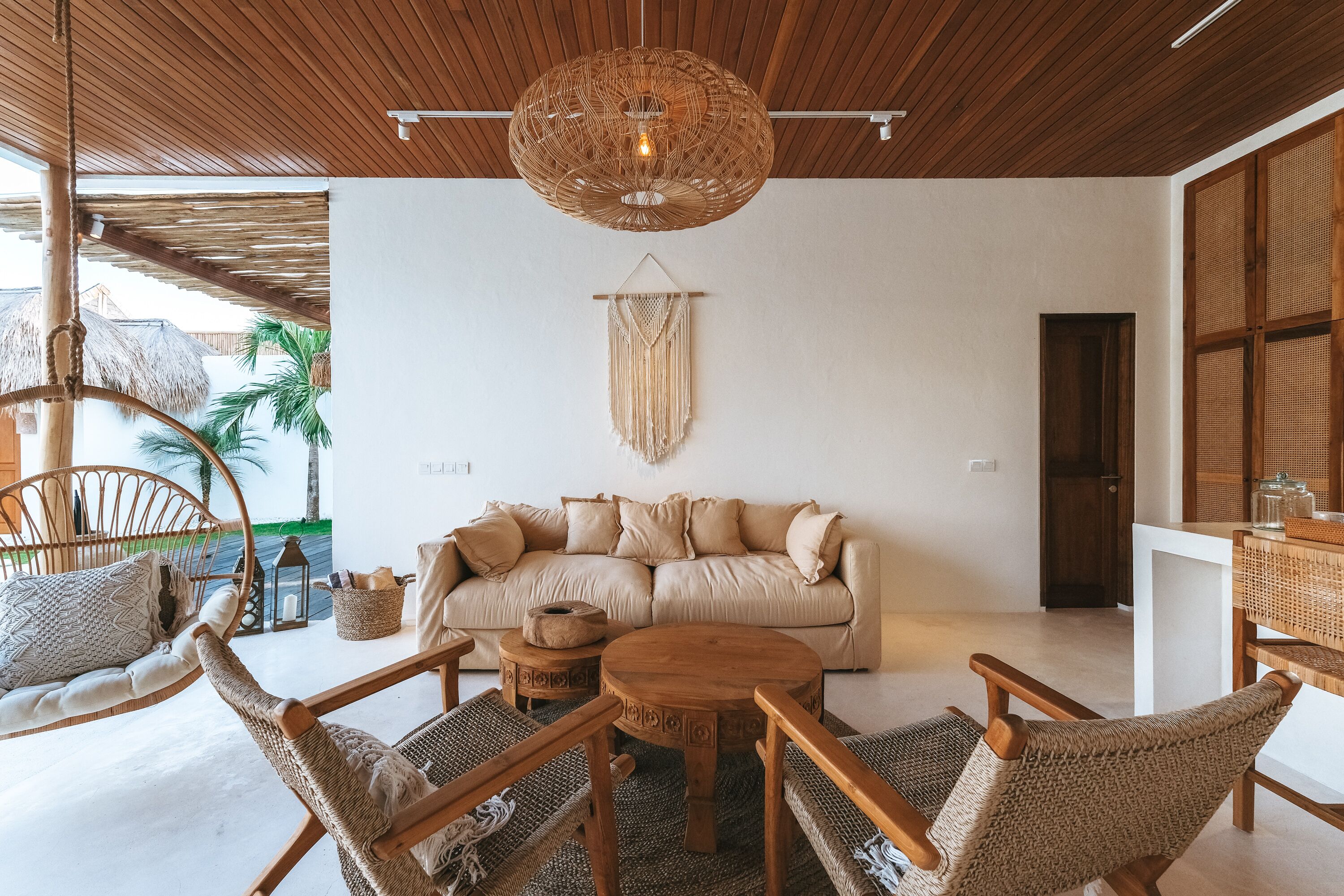 A cozy living room with a rattan sofa, wooden chairs, a round coffee table, and a hanging light fixture.