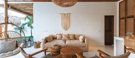 A cozy living room with a rattan sofa, wooden chairs, a round coffee table, and a hanging light fixture.