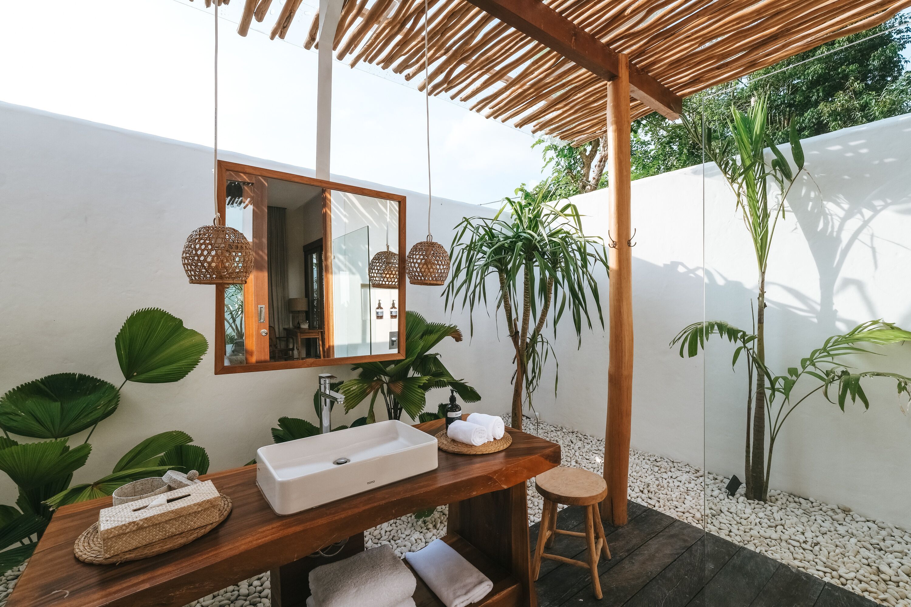 Un baño moderno con tocador de madera, un espejo grande y un lavamanos. Hay plantas y un taburete pequeño.