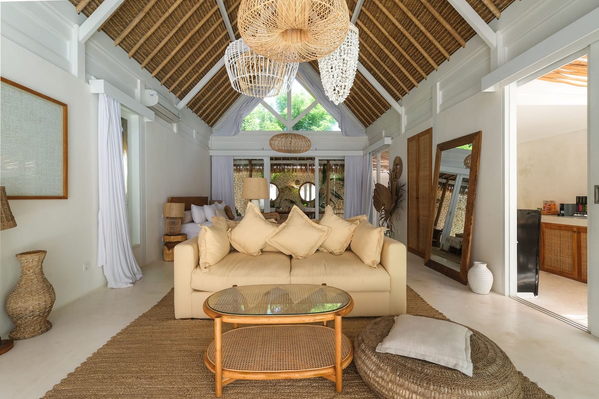 A spacious living room with a high ceiling, a large sofa, a glass coffee table, and a woven rug.