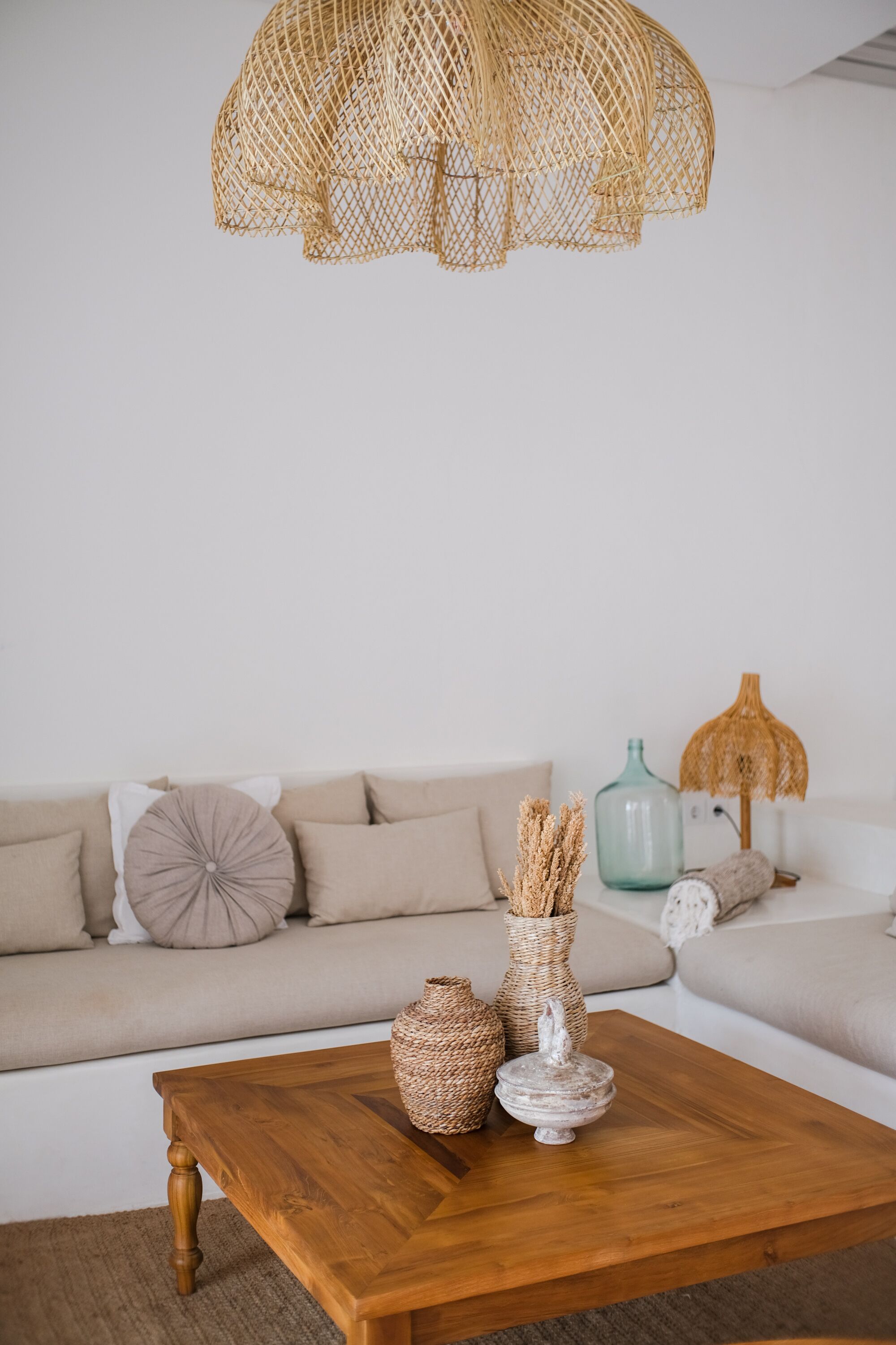 Una sala de estar con una mesa de centro de madera, un sofá color beige y una lámpara de techo trenzada.