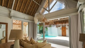 Amplia sala de estar con un sofá grande, una mesa con lámpara y vista a una piscina a través de amplios ventanales.