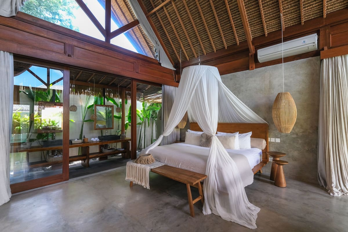 A bedroom with a canopy bed, wooden furniture, and a view of greenery outside.