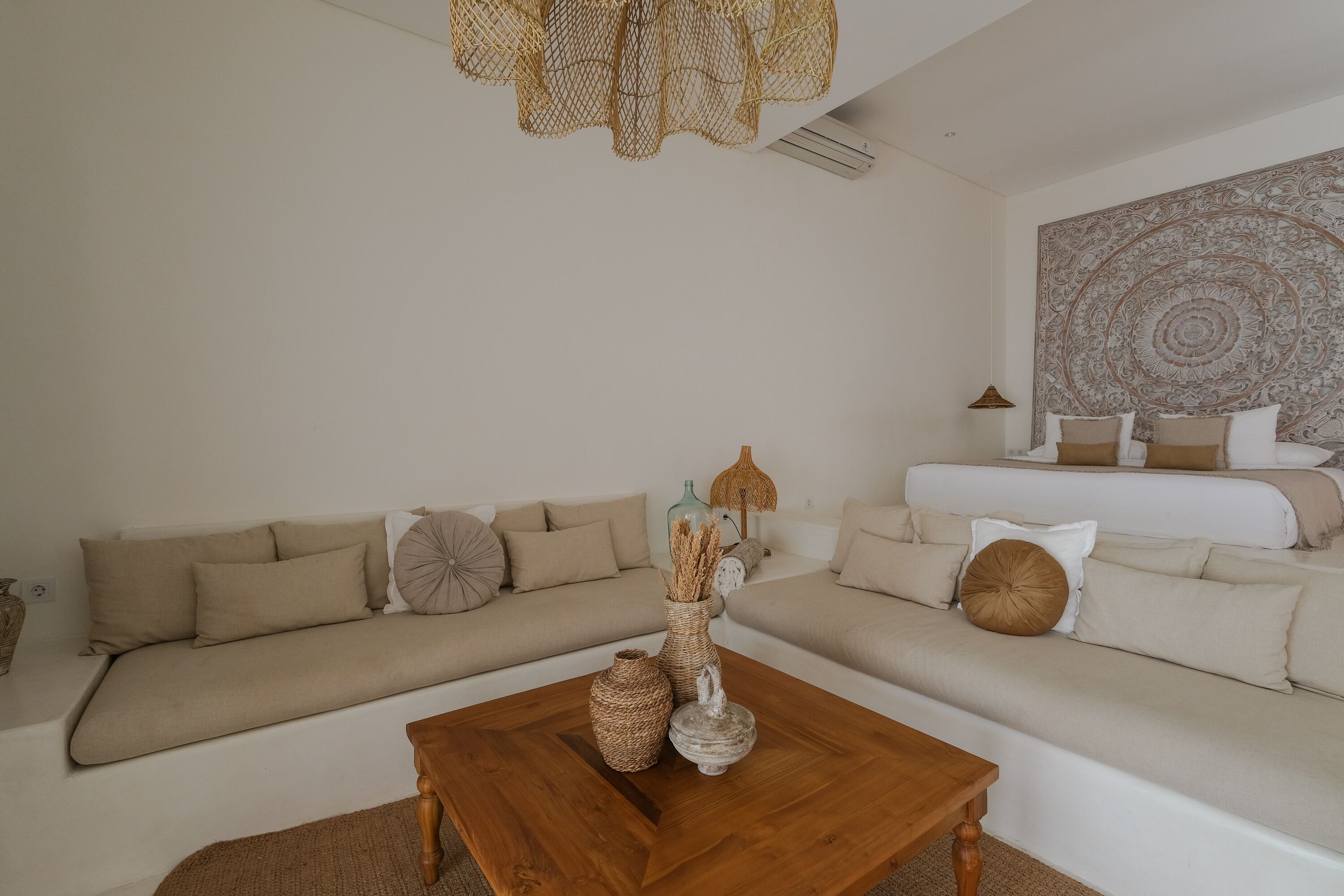 A modern living room with a wooden coffee table, beige sofas, and a large tapestry on the wall.