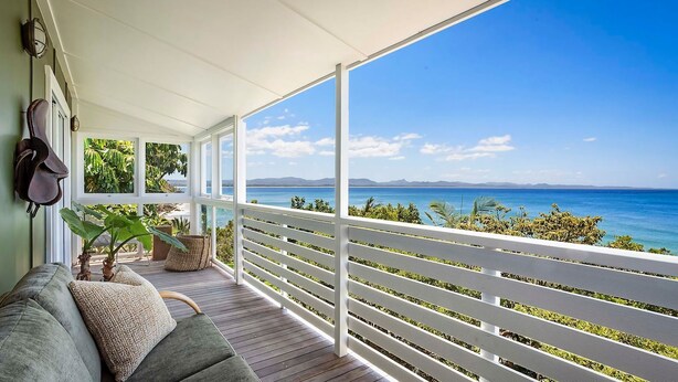 A covered balcony with a view of the sea, a sofa, and potted plants.