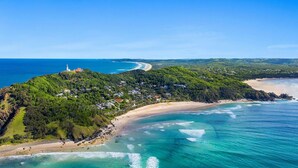 An aerial view of a coastal area with a beach, a lighthouse, and a residential area with houses and greenery.