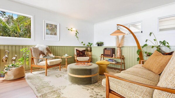 A cozy living room with a green wall, a large window, and a variety of plants.