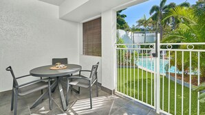 Ein Balkon mit Tisch und Stühlen, im Hintergrund ein Pool und Blick auf Palmen.
