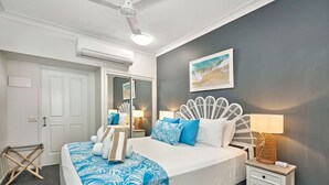 Ein Schlafzimmer mit Bett, Nachttischen, Deckenventilator, Wand-Klimaanlage, einer Tür und einem gerahmten Bild an der Wand.