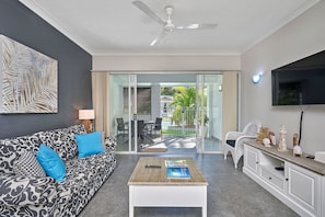 Relax in this stylish living room with a sofa, coffee table, and flat-screen TV, plus a door leading to a pool and lush outdoor space.