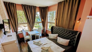 Una habitación acogedora con una cama, un escritorio y una silla. Cuenta con ventanas con cortinas, un televisor y vistas al exterior, con zonas verdes.