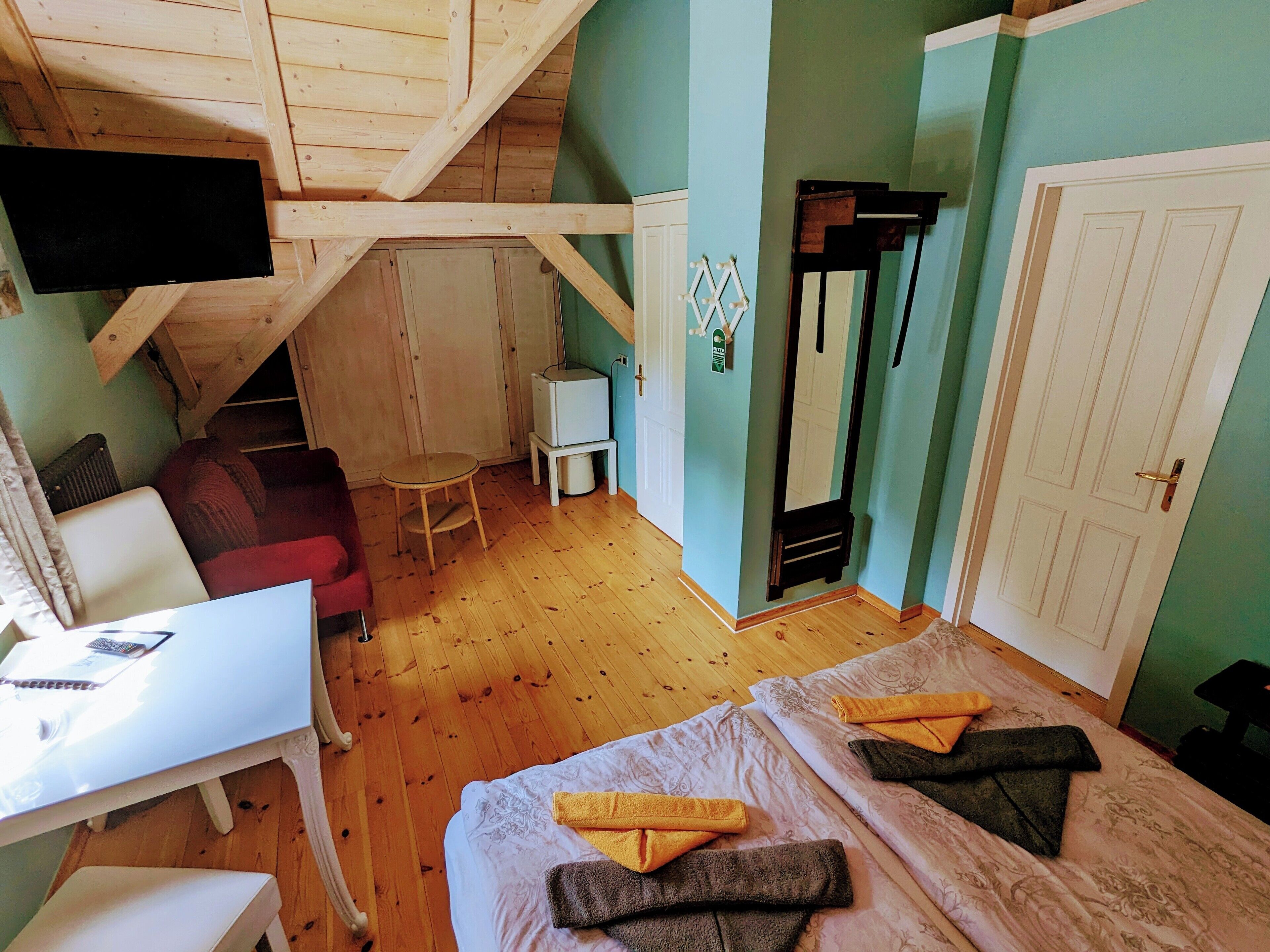 Ein Zimmer mit Bett, Schreibtisch, Stuhl, kleinem Tisch und Spiegel.
