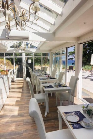 A sunlit dining area with white furniture, a chandelier, and a view of the outdoors. - Strandhotel Lindequist (Sellin)