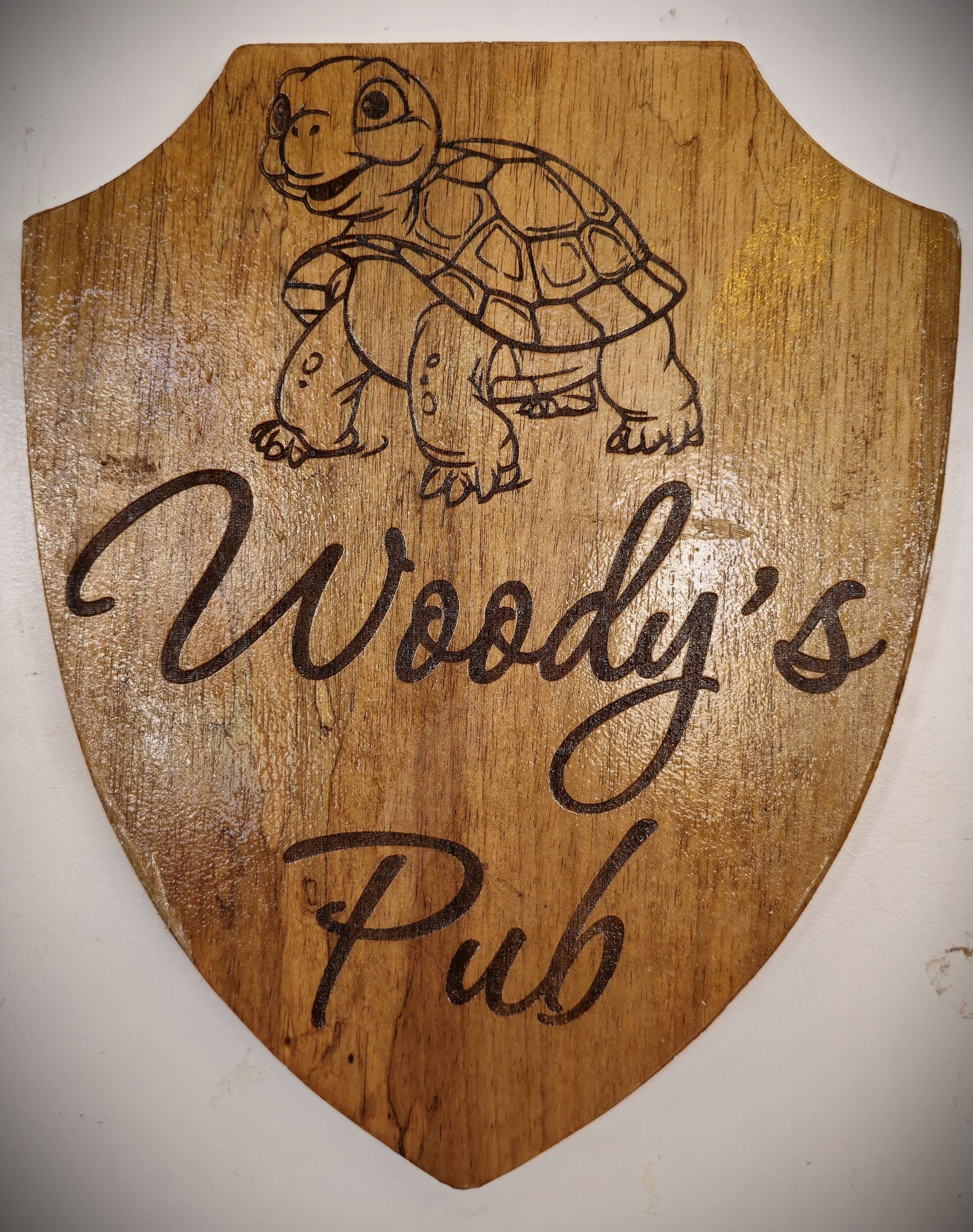 A wooden plaque with a turtle illustration and the text "Woody's Pub".