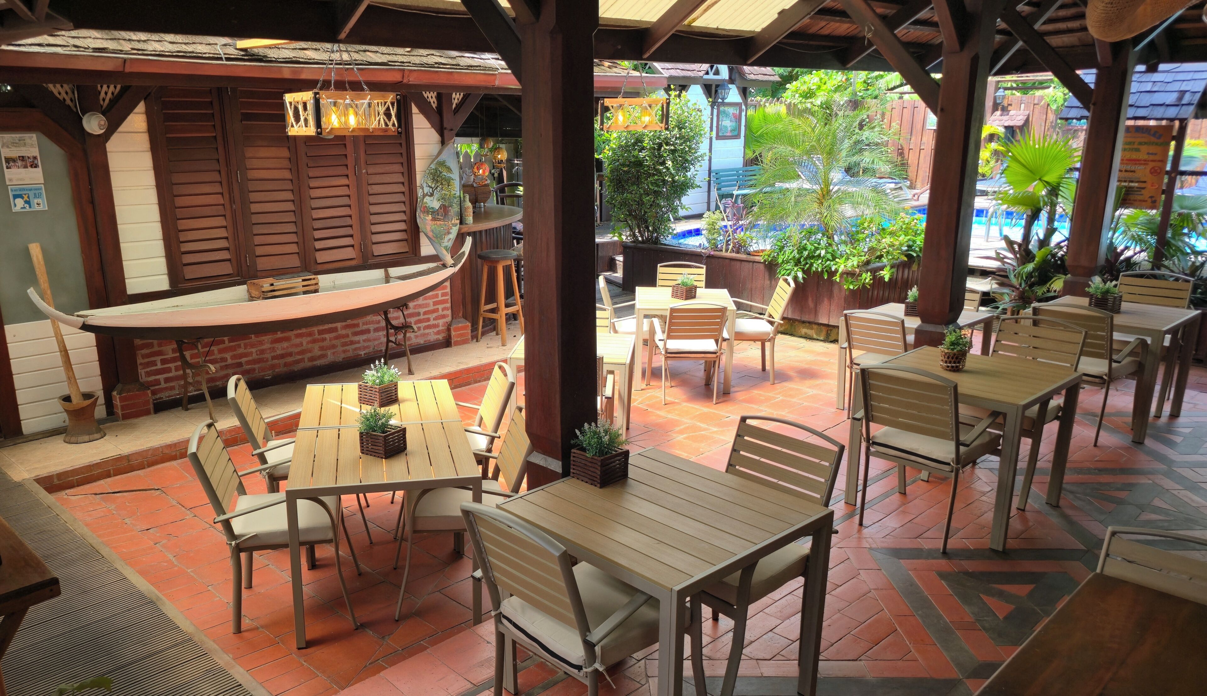 Un patio al aire libre con mesas y sillas de madera, una zona de bar y plantas en macetas.