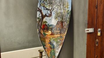 A wooden barrel with a painted depiction of a tree and landscape, placed against a wall with a door.