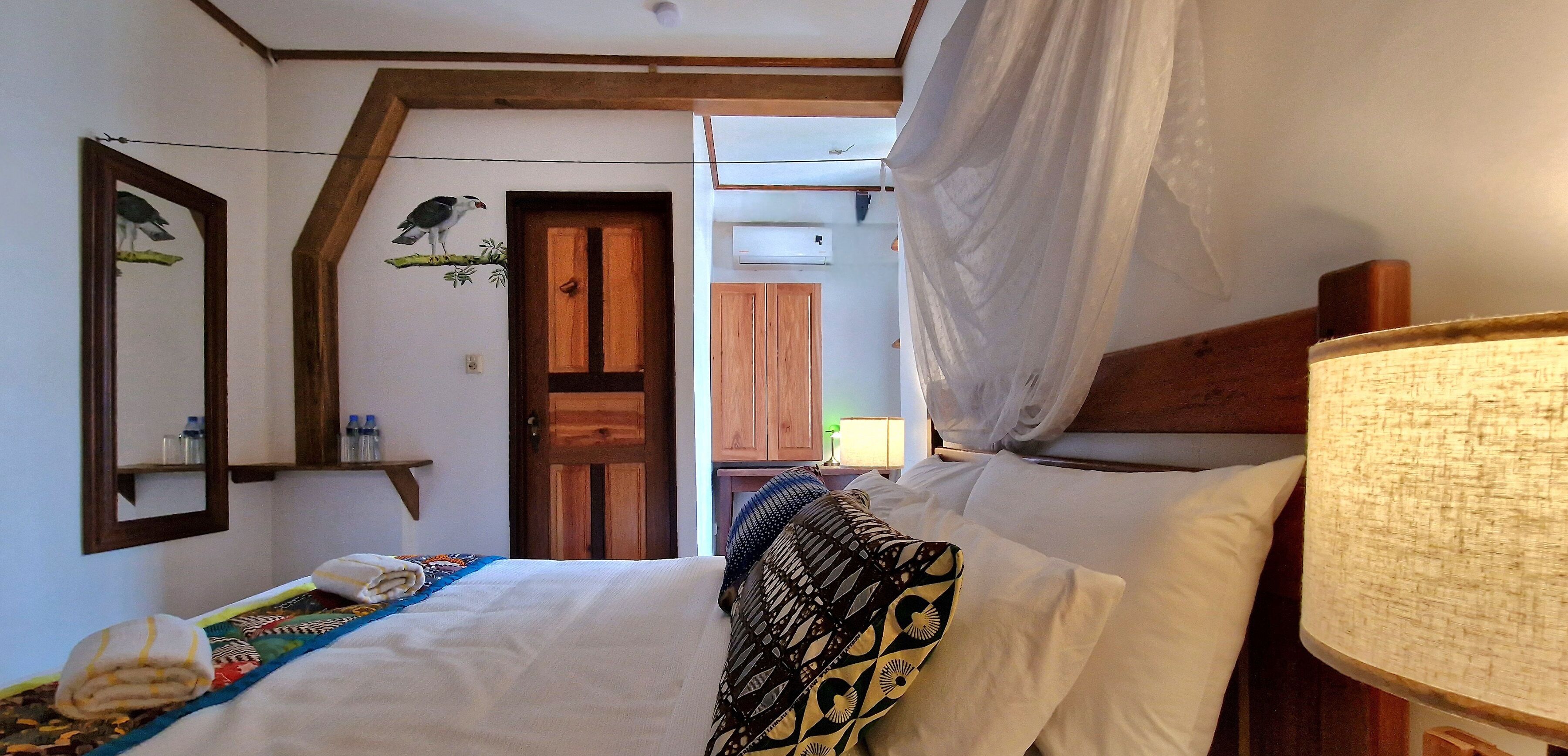 A bedroom with a bed, a nightstand, a lamp, a wooden door, and a mirror.