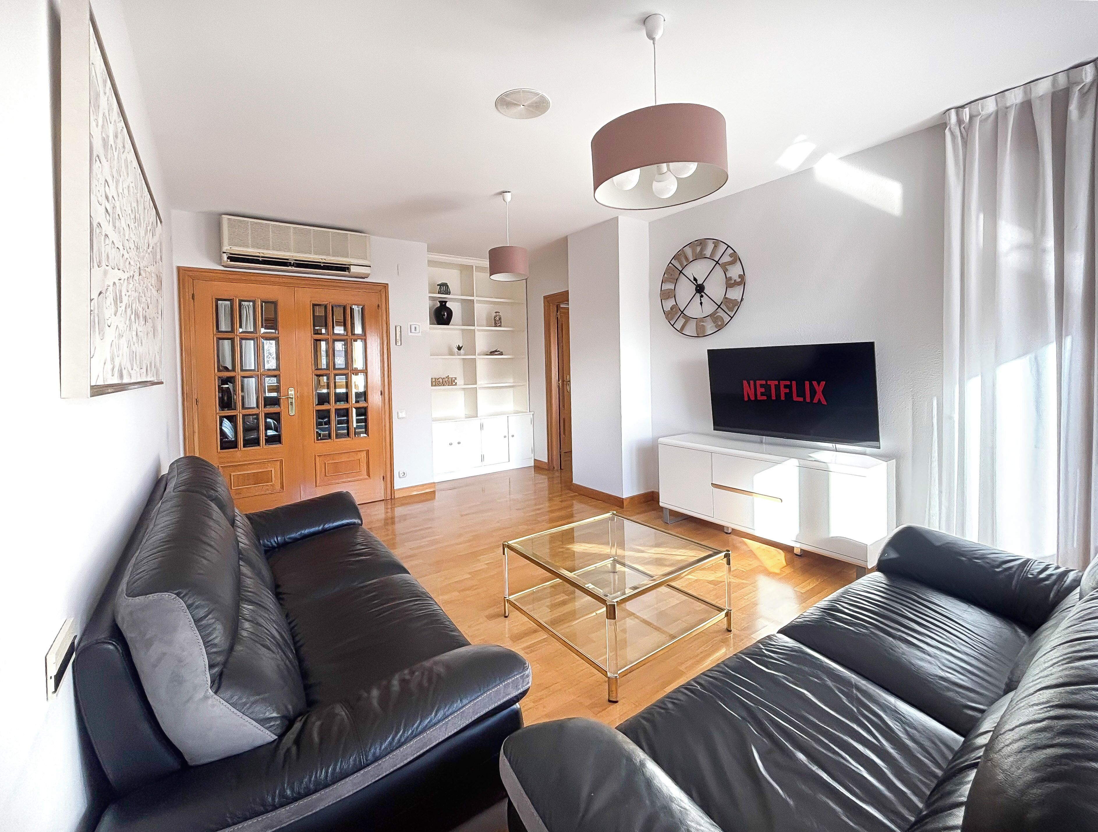 Een moderne woonkamer met een leren bank, een glazen salontafel, een televisie en een boekenkast.