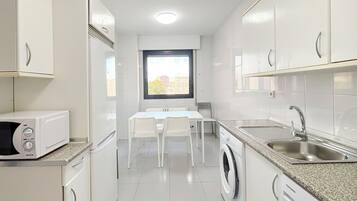 A compact kitchen with white cabinets, a microwave, a washing machine, and a dining area with a table and chairs.