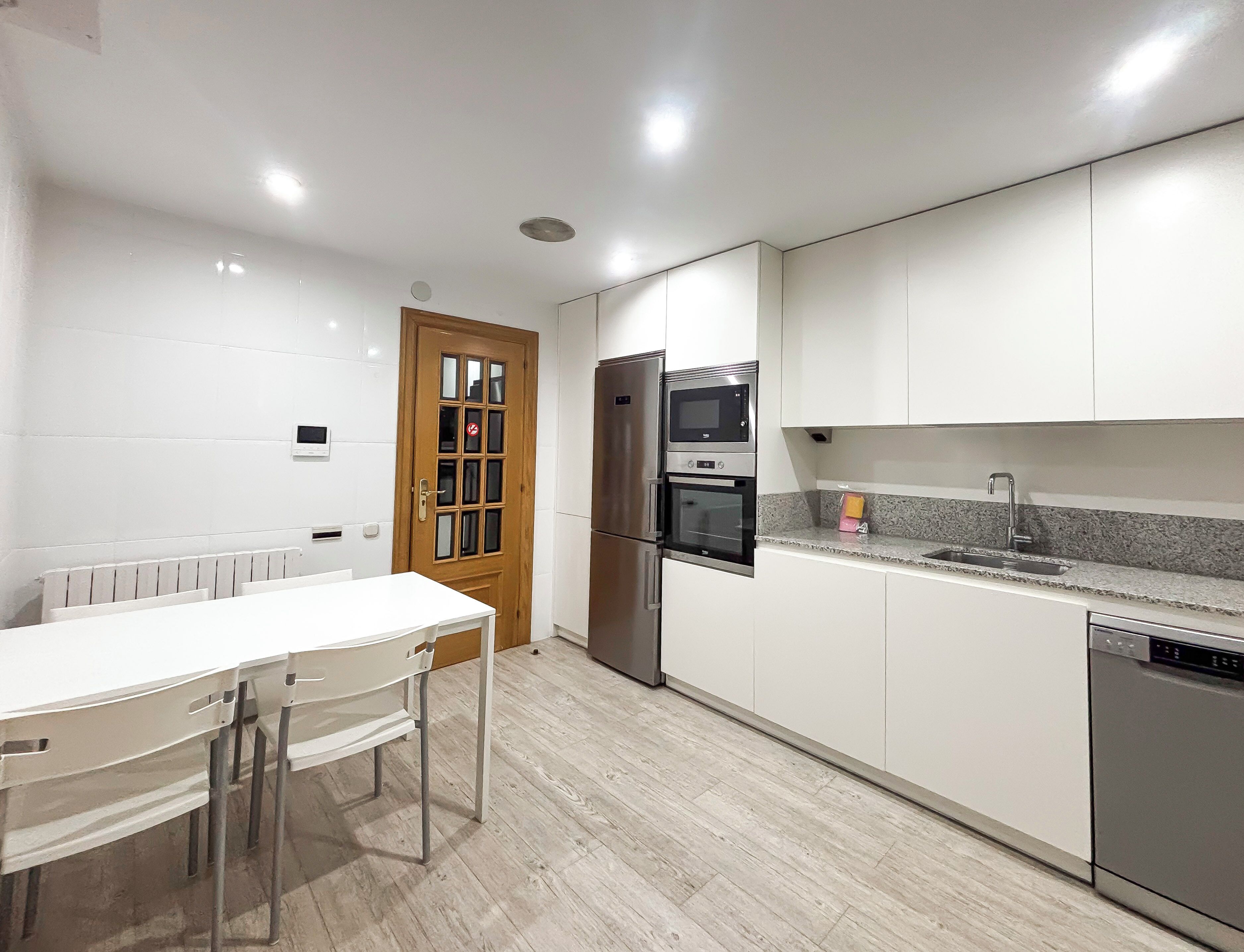 A modern kitchen with white cabinets, a stainless steel refrigerator, an oven, a microwave, a granite countertop, and a white dining table with chairs.