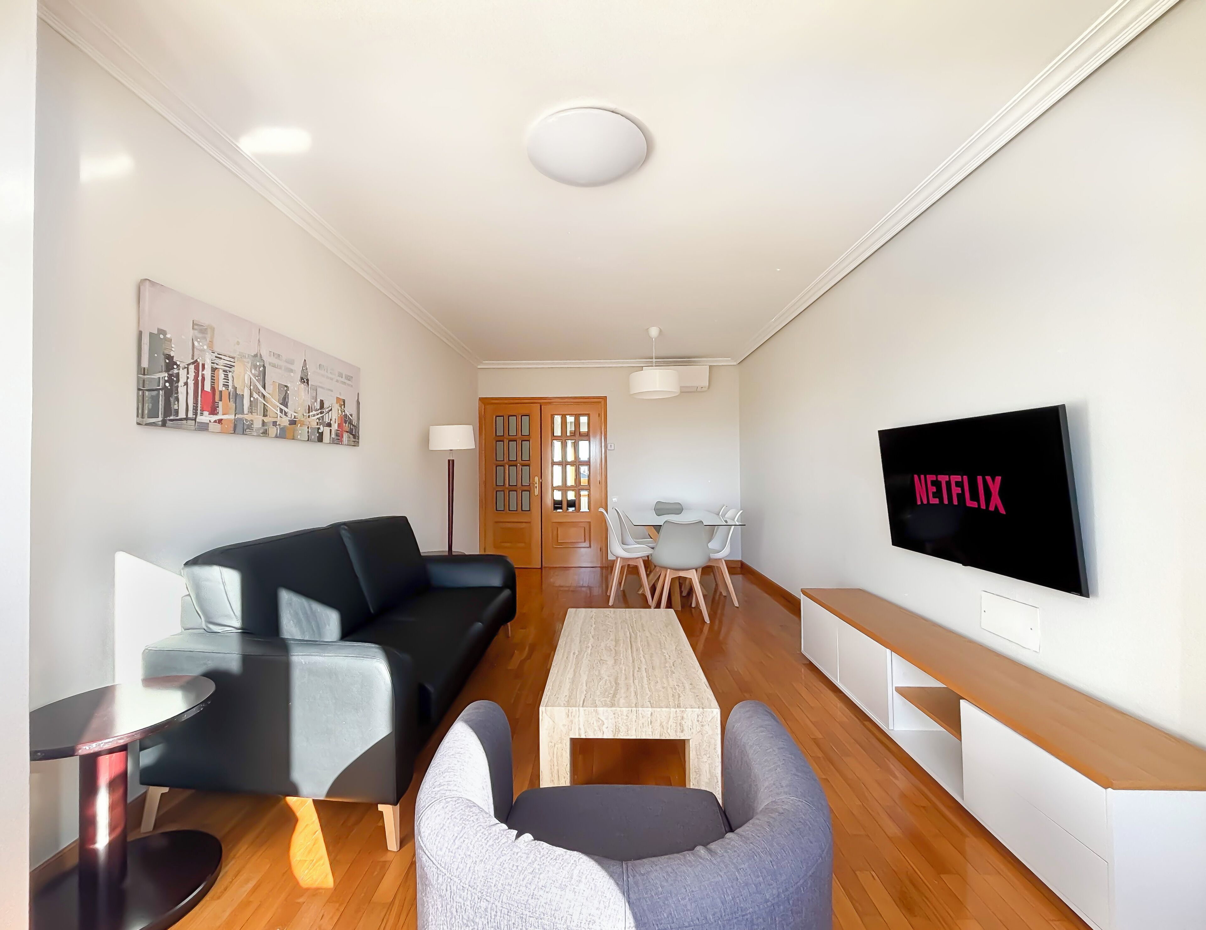 Una sala moderna con un sofá, sillas, una mesa de centro, un televisor y un comedor.