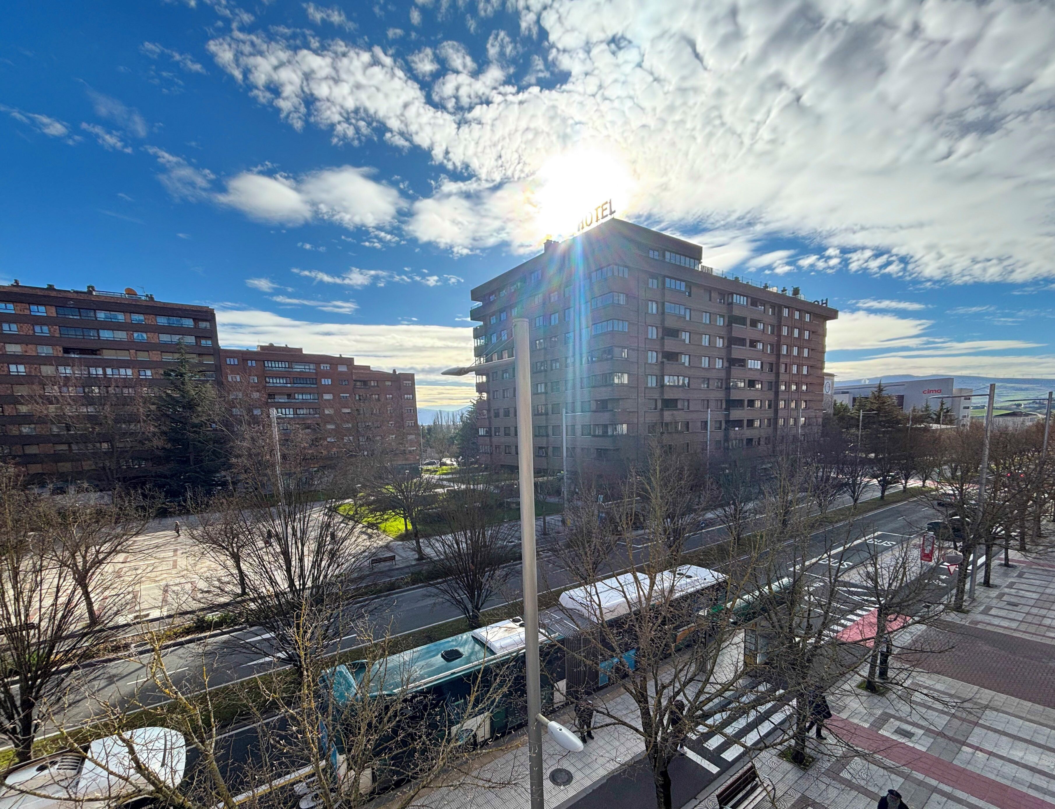 Um hotel com vários andares e uma torre central, cercado por outros edifícios, uma área de estacionamento e uma passarela.