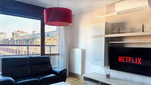 A modern living room with a leather sofa, a white coffee table, a red pendant light, a TV with 'NETFLIX' on the screen, and a view of a bridge through the window. - Apartamentos Gestión de Alojamientos (Pamplona)