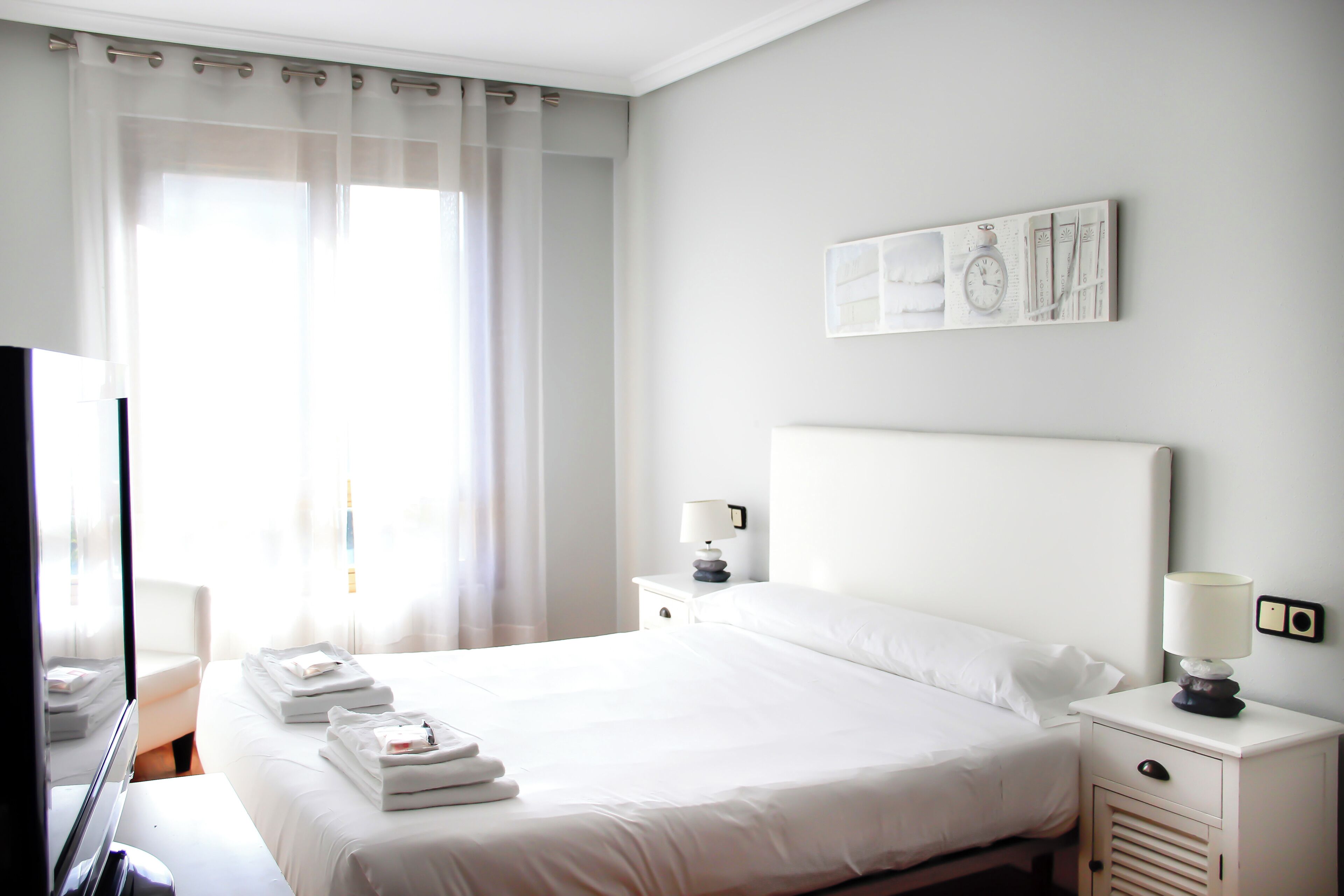 A hotel room with a bed, bedside tables, a TV, and a window with curtains.