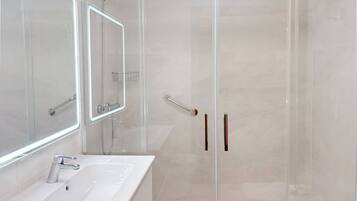 A modern bathroom with a glass-enclosed shower, a white sink, and a large mirror.