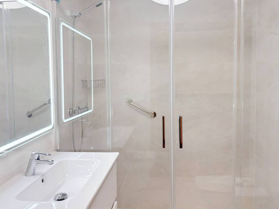 A modern bathroom with a glass-enclosed shower, a white sink, and a large mirror.