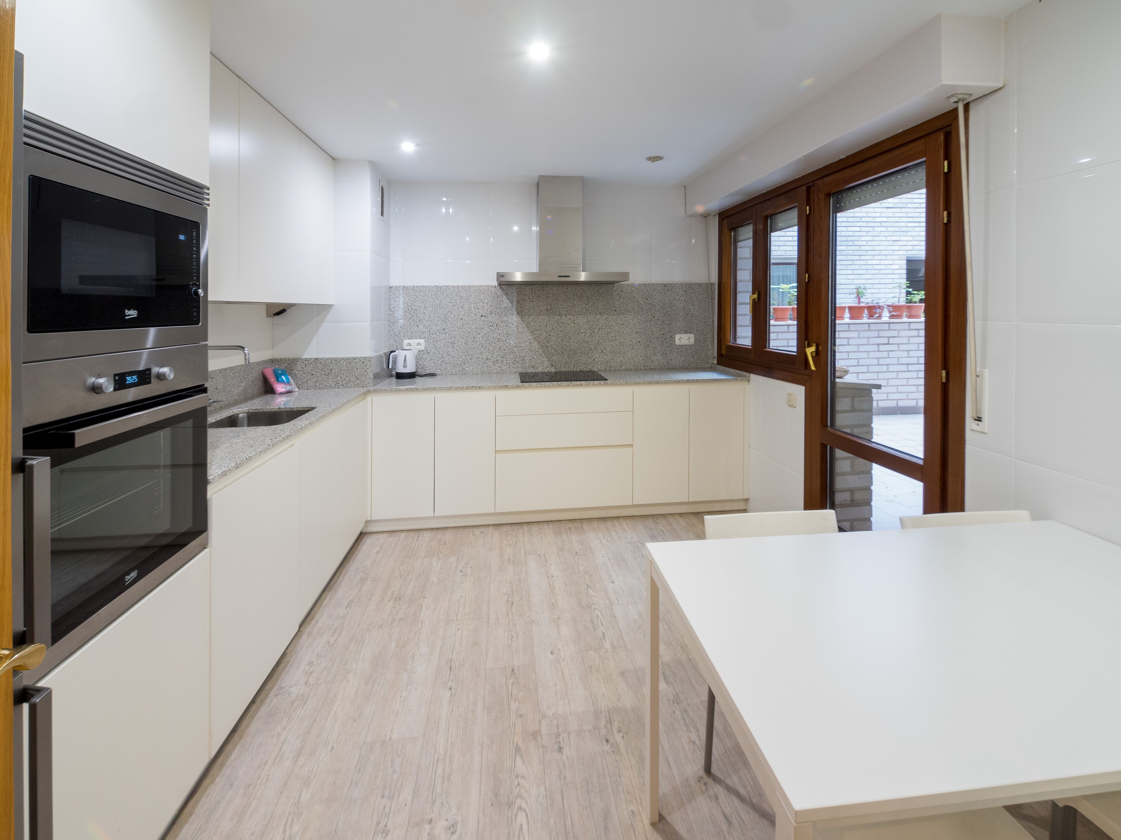 A modern kitchen with white cabinets, a built-in oven, a microwave, a granite countertop, and a window with a view of the outside.