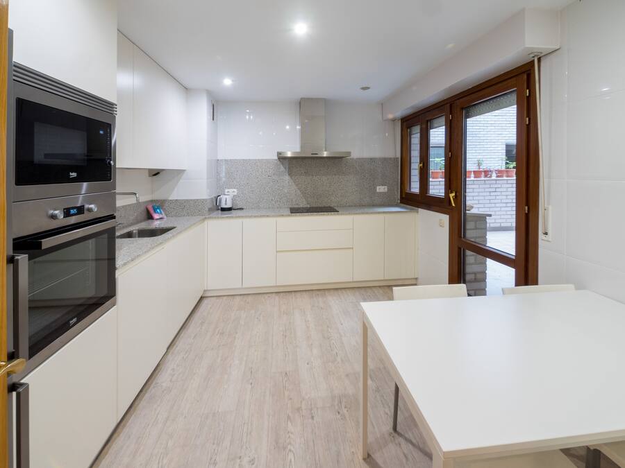 A modern kitchen with white cabinets, a built-in oven, a microwave, a granite countertop, and a window with a view of the outside.
