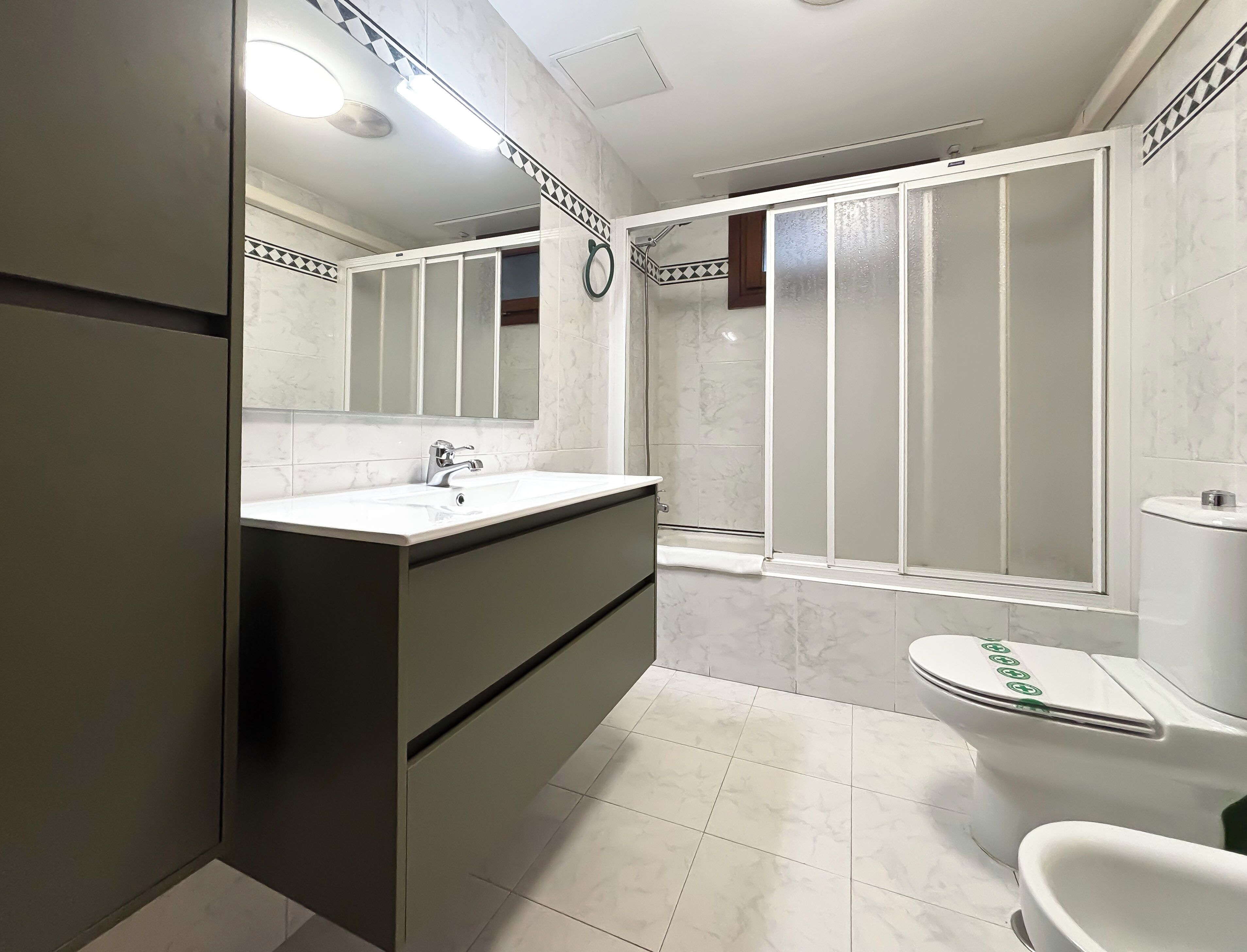 Un baño con lavamanos blanco, un espejo, inodoro y cabina de ducha.
