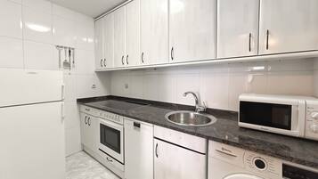 A modern kitchen with white cabinets, a stainless steel sink, a built-in oven, a dishwasher, a microwave, and a washing machine.