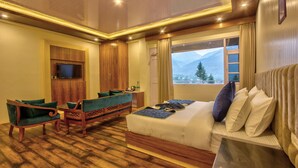 Habitación de hotel con cama, sofá, televisión y ventana con vista a la montaña.