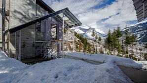 Un espacio exterior cubierto de nieve con un edificio que tiene una escalera metálica y un porche cubierto.