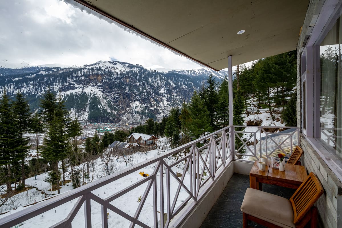 Un balcón con vistas a montañas nevadas, una mesa de madera con sillas y una barandilla.