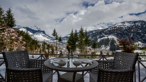 Una mesa redonda con cuatro sillas y un florero, frente a un paisaje de montañas y árboles cubiertos de nieve.