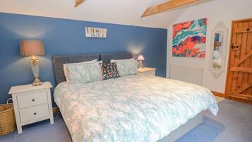A bedroom with a bed, two nightstands, a lamp, a colorful abstract painting, a mirror, and a wooden door.