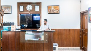 A reception desk with a clock, framed artwork, and a sign indicating CCTV surveillance. -  SKS Excel Inn (Gurugram)