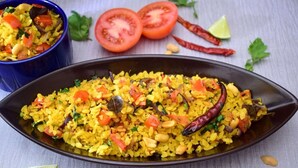 A dish of yellow rice with vegetables and spices, served on a black plate. -  SKS Excel Inn (Gurugram)