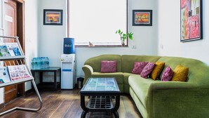 A room with a green sofa, a coffee table, a water dispenser, framed artwork, and a window with a view. -  SKS Excel Inn (Gurugram)