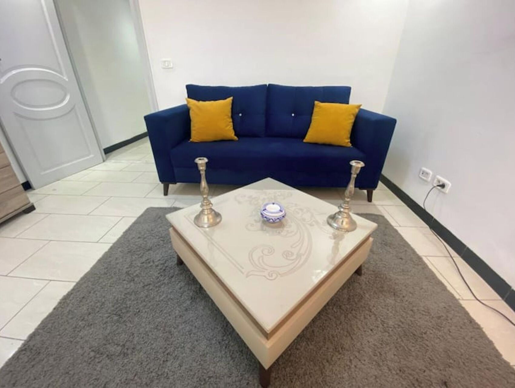Una sala de estar con un sofá azul, dos cojines amarillos y una mesa de centro decorativa con dos portavelas.