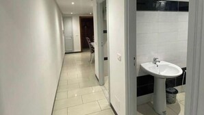 A corridor with a tiled floor, a white sink, and a trash bin.