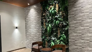 A room with a herringbone-patterned floor, two wooden chairs, a small round table, and a vertical wall with a textured pattern and a green plant wall. - Esma Family GuestHouse (Malang)
