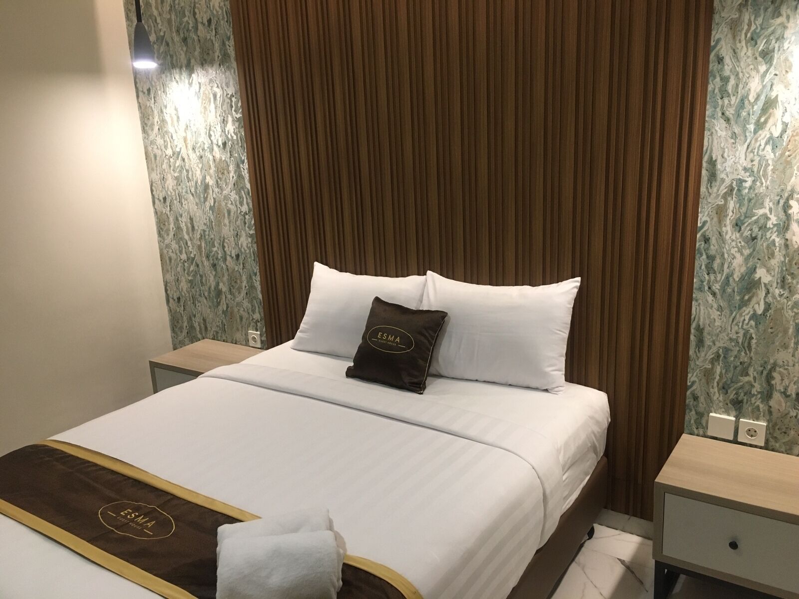 Een hotelkamer met een net opgemaakt bed, een houten hoofdeinde en een wand met een marmerlook.