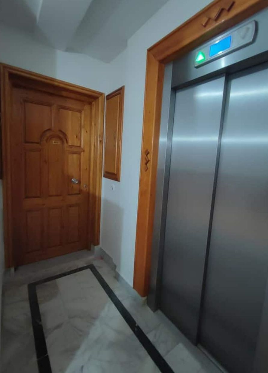 Een gang met een houten deur en een lift.