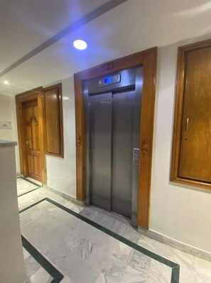 A hallway with a marble floor, wooden doors, and a modern elevator.