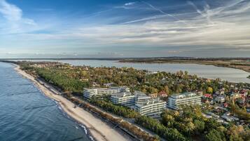 Vista aérea de uma área costeira com praia, edifícios residenciais e um corpo de água.
